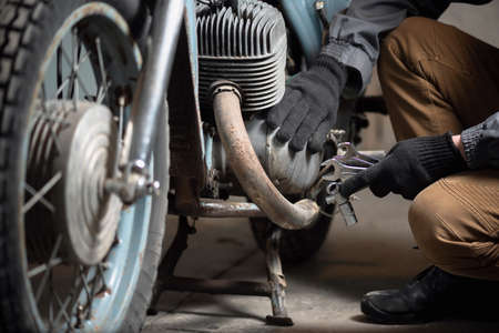 A mechanic with a wrenches in hand is sitting on the broken motorbike background. Motorcycle repairing service concept.の写真素材
