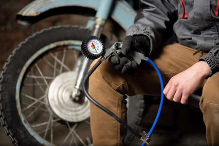 A tire fitting service worker is sitting with a car tyre inflation gun on a motorbike wheel background.の写真素材