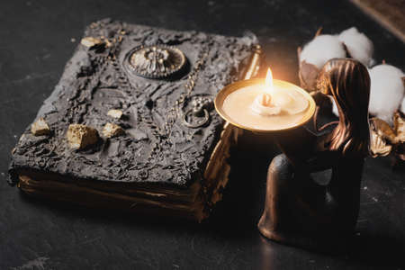 Ancient magic book and burning candle on the table close up. The witchcraft concept.