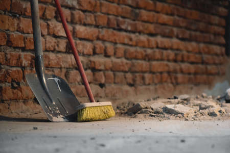 Shovel and broom on the dusty construction site floor background.