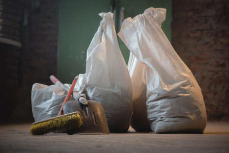 Shovel, broom and bags with a construction garbage on the dusty construction site floor background.の写真素材
