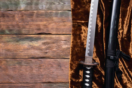 Katana sword on the golden cloth on the brown wooden table background with copy space.