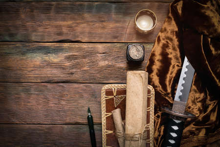 Katana sword and ancient paper scroll on the brown wooden table background with copy space.