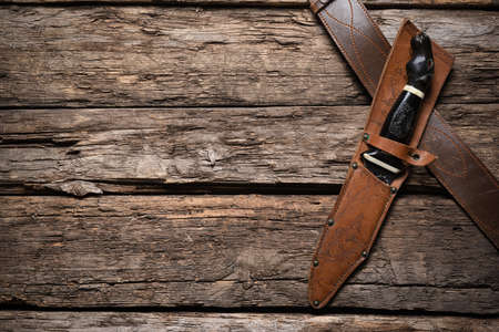 Hunting knife and leather case on the old wooden table background. Hunter accessory concept...