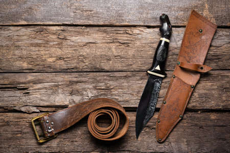 Hunting knife and leather case on the old wooden table background. Hunter accessory concept background with copy space.の写真素材