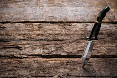 Hunting knife stuck in the old wooden table background with copy space.の写真素材