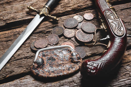 Pirate weapon and ancient coins on the old wooden table background. Piracy.の写真素材