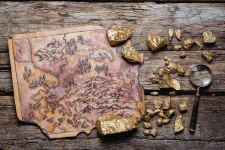 Ancient pirate treasure map and golden ore on the wooden flat lay table background.の写真素材