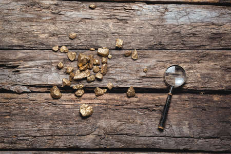 Golden ore and magnifying glass on the old wooden table flat lay background. Golden mine concept.