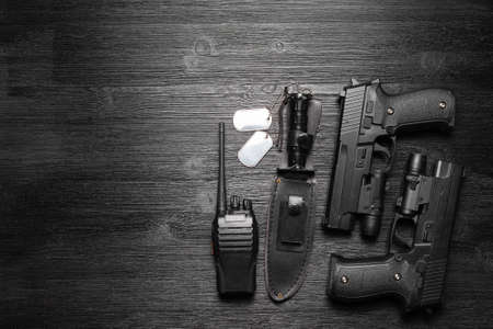 Black airsoft gun, walkie talkie radio station and knife and soldier badge on the black flat lay...