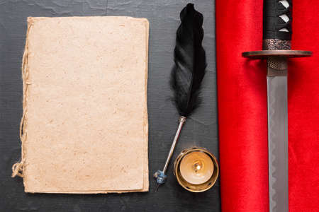 Samurai story concept. Empty book with blank pages, quill pen and a katana sword flat lay background.の写真素材