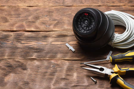 Security cctv camera, screewdriver, wire and pliers on the wooden workbench background with copy...