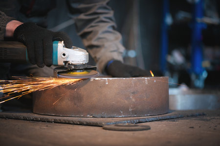 Man is polishing a metal pipe by angle grinder saw.