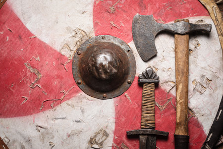 Old sword battles, ax and shield on the wooden table top view background with copy space.の写真素材
