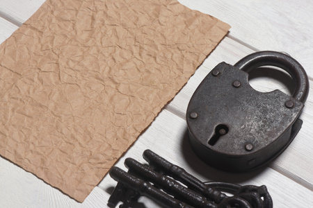 Old padlock and blank crumpled paper sheet page on the wooden desk table background. Top view. Secret information concept. Looking for the answers. Searching of clues concept. Agreement trap.の写真素材