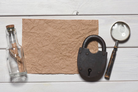 Message scroll letter in the bottle, magnifying glass and blank crumpled blank paper sheet with copy space on the white wooden desk table flat lay background. Ancient map concept.の写真素材