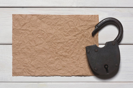 Old padlock and blank crumpled paper sheet page on the wooden desk table background. Top view. Secret information concept. Looking for the answers. Searching of clues concept. Agreement trap.の写真素材