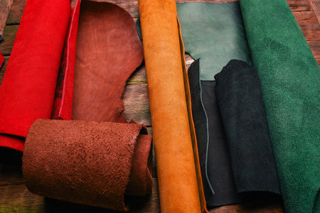 Colorful pile of leather rolled up pieces on the tanner table top view. Leather craft concept...