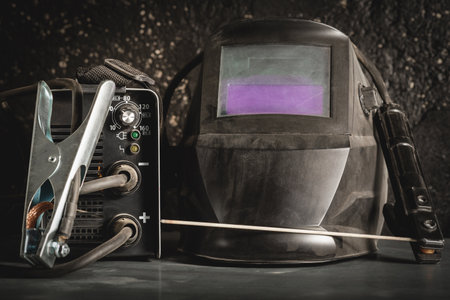 Welding helmet and welding inverter machine with electrode close up on the metal workbench...