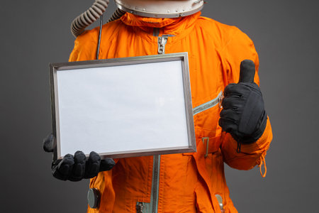 Astronaut holding in hand a blank diploma certificate with copy space. Space message. Space program goals template.の写真素材
