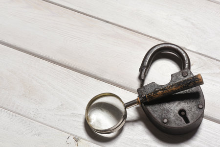 Old padlock and magnifying glass on the wooden desk table background. Secret information concept....