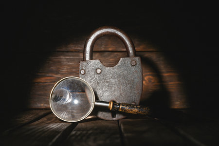 Old barn padlock and magnifying glass on the wooden desk table background close up. Secret information concept. Looking for the answers. Searching of clues concept.の写真素材