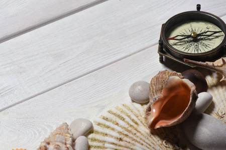 Vintage compass, seashells and pebble stones on the white wooden desk table close up background with...