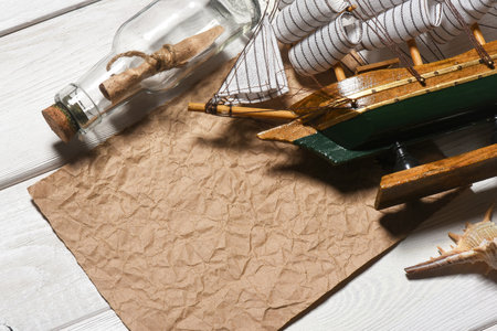 Message scroll letter in the bottle, sea ship and blank crumpled blank paper sheet with copy space on the white wooden desk table flat lay background. Ancient map concept.の写真素材