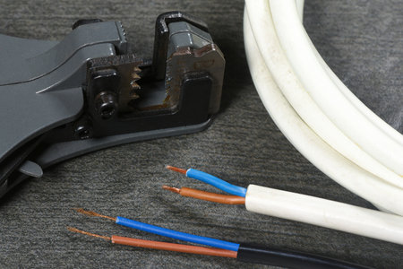 Wire stripper and electrical cable on gray workbench background close up.