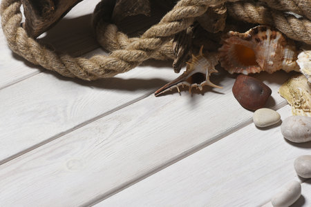 Seashells, mooring rope and pebble stones on the white wooden desk table background top view. Sea travel flat lay concept background with copy space.の写真素材