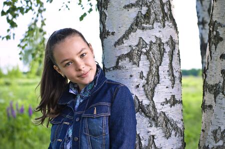 Girl standing near birch tree in summer tilting her head and smilingの写真素材