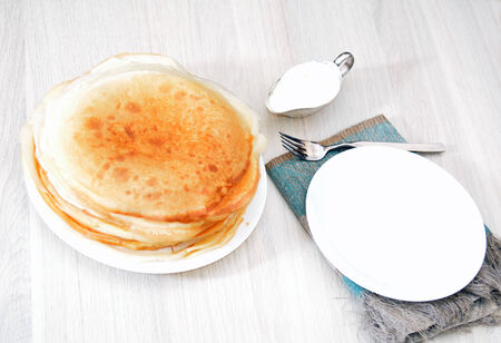 Stack of pancakes on the table with sour cream and an empty plateの写真素材