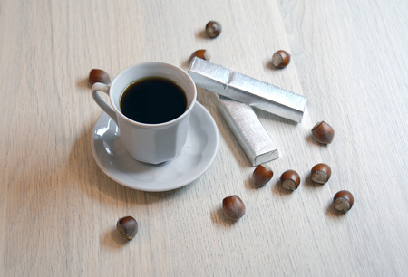 Cup of black coffee and two hazelnut chocolates with nuts scattered on the tableの写真素材