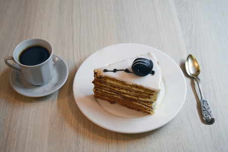 piece of white chocolate cake on a saucer with a cup of coffee and a spoonの写真素材