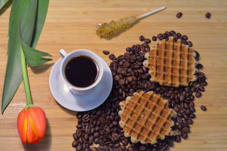 cup of strong black coffee with a fresh flower and two round multigrain waffles on coffee beansの写真素材