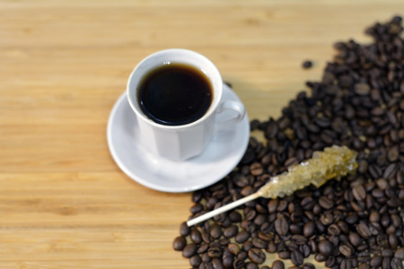 cup of black coffee with a sugar stick on top of coffee beansの写真素材