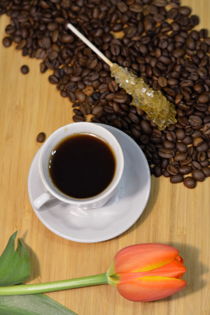 coffee in a white cup, fresh tulip and coffee beans with a sugar stick on topの写真素材