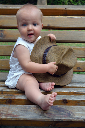 an infant sitting on the bench with the hat in her handsの写真素材