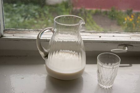 Jug of milk and a glass on a windowsill with the building behindの写真素材