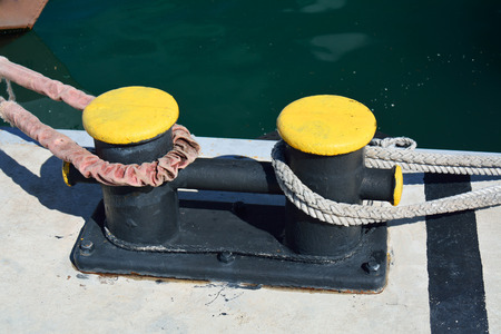 Dyed metal bitt with a velvet rope and a plain mooring line next to the seaの写真素材