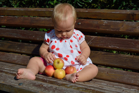 a cute 11 months infant girl playing with apples on the benchの写真素材