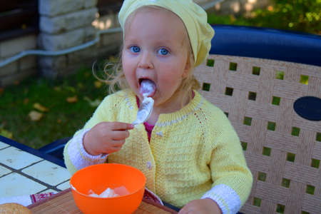 toddler girl eats sour cream with a spoon on the tableの写真素材