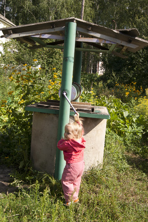 iron old well and a toddler girl next to itの写真素材