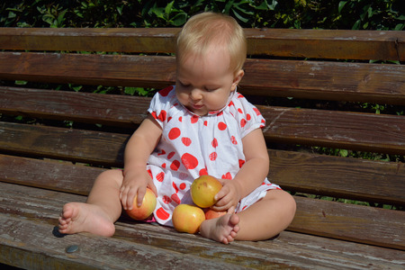 A baby girl collecting apples on the benchの写真素材