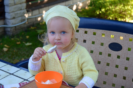 girl sits in a chair and eats sour cream with a spoonの写真素材