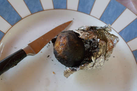 baked potato in foil with a knife ready to cutの写真素材