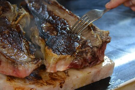 Meat chop on the salt plate, with a fork and a handの写真素材