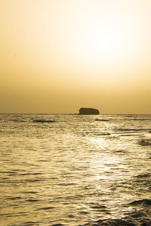 sunset on the seashore, with a big rock in the farの写真素材