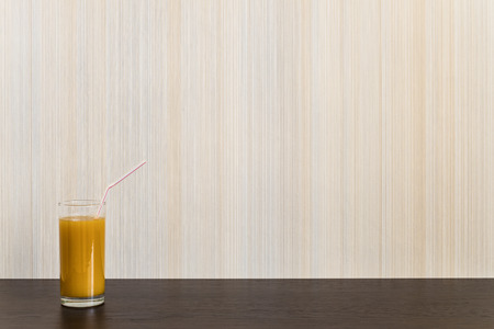 Glass of juice with straw on a wooden surface wenge color on the background wall with texture in a vertical strip. Minimalism. Background with copy space.の写真素材