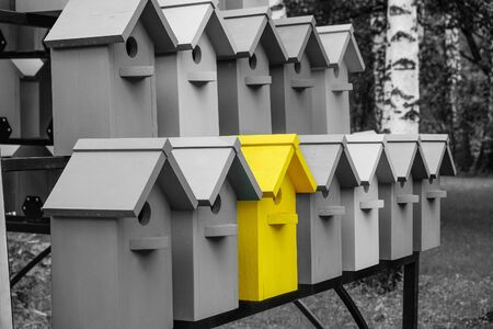 Yellow color wooden birdhouse stand out from the crowd. Metaphor to business concept. Stands out among the gray of similar objects. Notable among the competitors.の写真素材